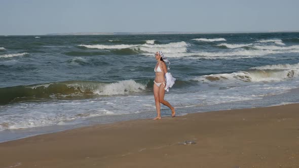 Brunette Woman in a White Swimsuit Walks Along a Sandy Beach