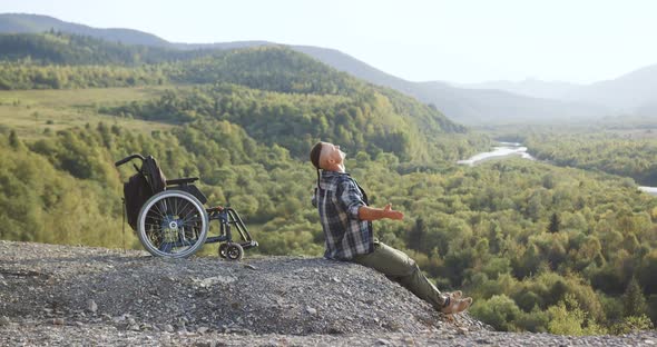 Likable Happy Smiling Young Disabled Man Relaxing on the Top of the Hill and Stretching His Hands in