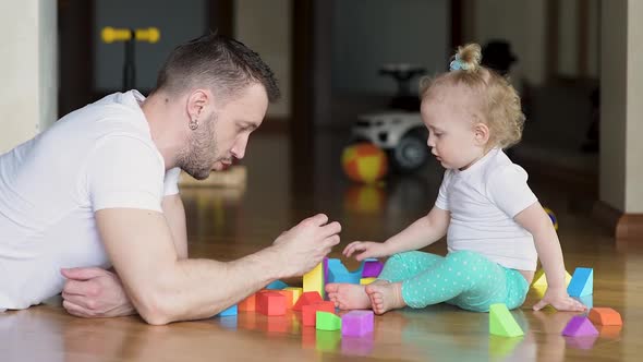 Dad plays with his daughter in colored pieces on the floor. Father and child alt