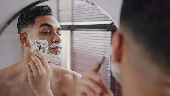Hispanic Arabian Arab Indian Bearded Handsome Man Shaving Using Disposable Razor in Bathroom Looking