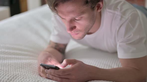 Handsome Young Man Using Smartphone in Bed 