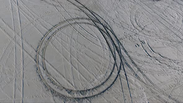 An aerial drone shot orbits a donut circle made by a car in the soft salt of the Bonneville Salt Fla