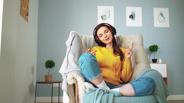 Girl in Headphones with Closed Eyes Relaxes on Cozy Sofa and Listens Music Home