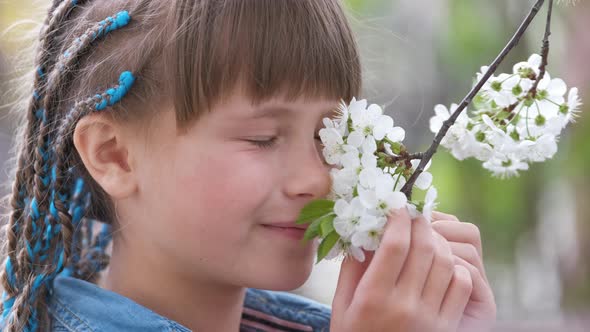 Happy Child Girl Playing in Spring Garden Enjoying Sweet Scent of White Cherry Tree Blossoming