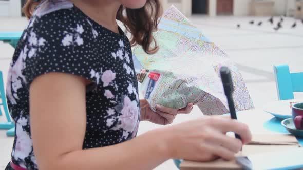 Beautiful Young Female Examining City Map, Writing in Notebook, Making Notes