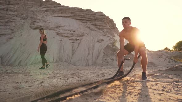 Athletic Man on Exercise Around the Sand Hills at Sunset Hits the Rope on the Ground