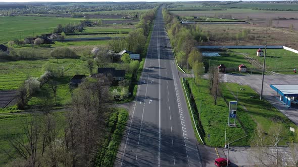 Aerial view of cars driving along the empty roadriding along trees and fields