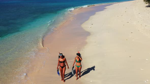Happy girls wearing snorkel set walking around white sandy beach washed by sea waves, trying to find