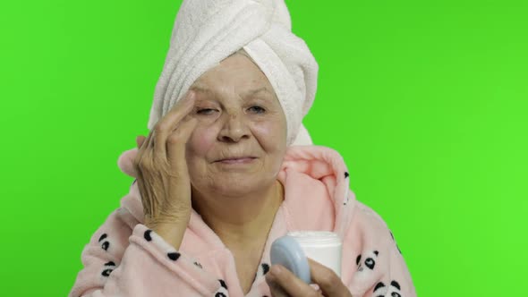 Elderly Grandmother in Bathrobe. Old Woman Applying Moisturizing Cream on Face