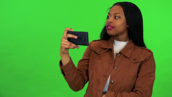 A Young Black Woman Takes Pictures of Something with a Smartphone - Green Screen Studio