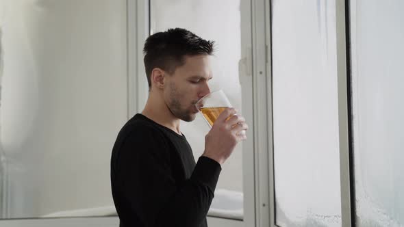 Caucasian Man with Large Cup of Tea Stands on Frozen Balcony on Sunny Day