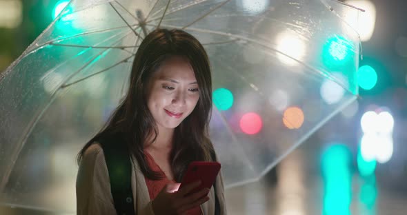 Woman hold with umbrella and use of mobile phone in the city at night