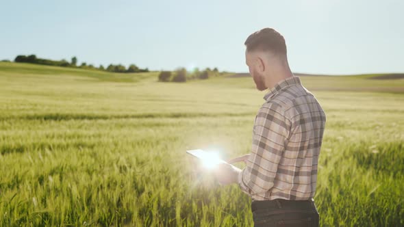 The Farmer is Standing Near the Field and Looking Through the Information on the Tablet