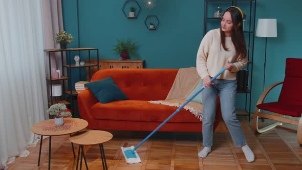 Joyful Young Woman is Mopping Floor in Apartment Living Room Having Fun Listening to Music at Home