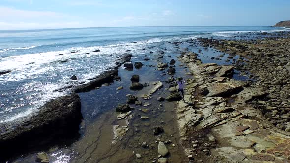 Aerial shot of young man running on a scenic rocky beach coastline.