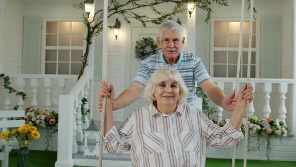 Senior Couple Together in Front Yard at Home. Man Swinging and Hugging Woman. Happy Mature Family