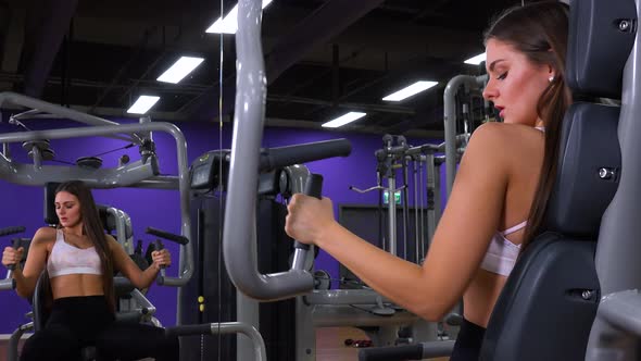 A Young Fit Woman Trains on a Machine in a Gym - View on the Reflection in a Mirror