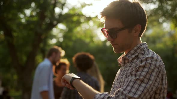 Caucasian Male in Plaid Shirt and Sunglasses Standing in Park Using Tablet Checking Time on Wrist