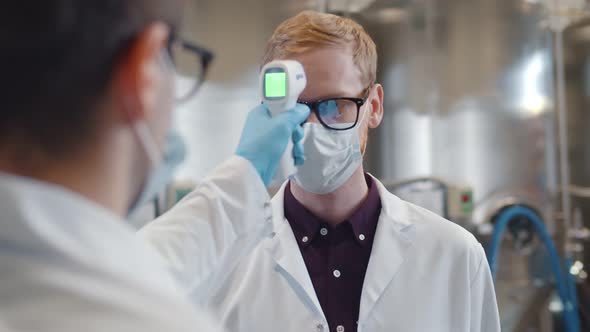 Close Up of Manager Measuring Body Temperature of Workers with Infrared Thermometer at Factory