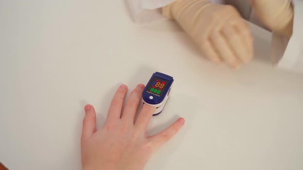 A Doctor in Latex Gloves Using a Pulse Oximeter Measures the Level of Oxygen in the Patient's Blood