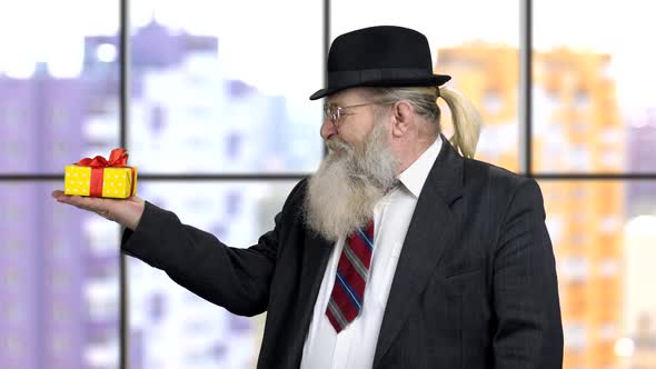 Old Businessman in Formal Suit Pointing at Gift Box