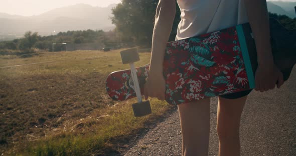 Closeup Woman Hands Holding Skate Longboard and Walk Along Meadow on Epic Sunset