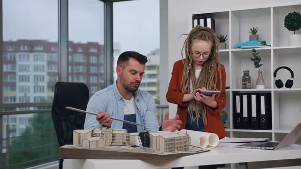 Man and Woman with Dreadlocks Working Together with Mock-up of New Buildings 