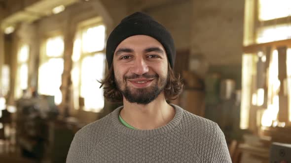 Young Multiethnic Male with Black Beard and Sock Cap Standing in Joinery and Looking at Camera