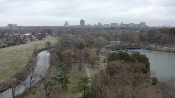 City park on dreary winter day, buildings in background. Aerial dolly forward