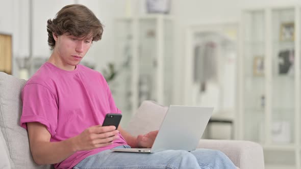 Casual Young Man Using Smartphone and Laptop at Home 