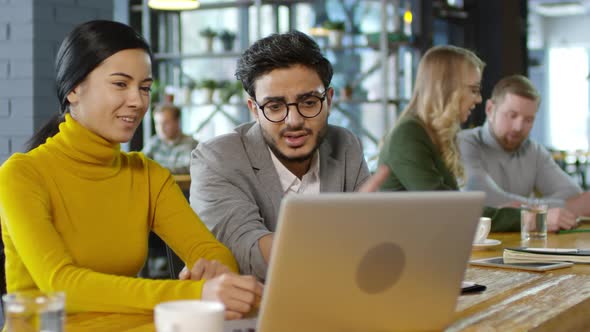 Young Multiethnic Coworkers Talking and Using Laptop in Cafe