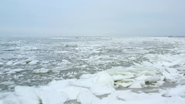 Drone flying fast, low and backwards over frozen lake that is thawing out in the late winter, early