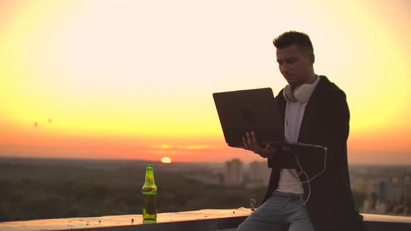 Hipster Man with a Laptop on the Edge of the Roof. Freelancer at Work. Wireless Mobile Internet. He