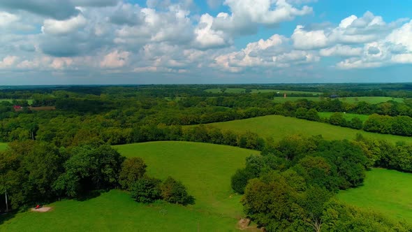 Flying past a barn and tractor over some farmland and trees with beautiful skies