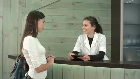 Smiling Spa Manager with Tablet Greeting Female Customer at the Reception Desk