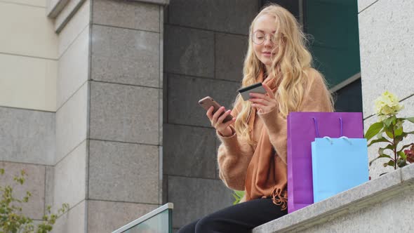 Attractive Female Shopper Makes Online Order Using Phone Caucasian Woman Holding Credit Card and