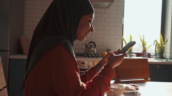 Cheerful Muslim woman texting by phone