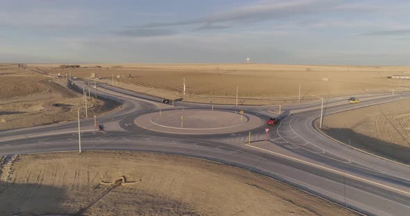 Cars and pickup trucks navigate a modern roundabout in the middle of the countryside.