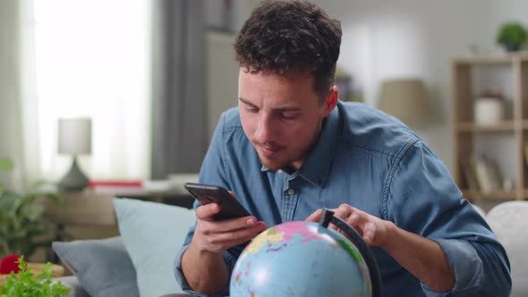 Young Man Looking for a Country for Tourism on the Globe at Home in the Living Room on the Sofa