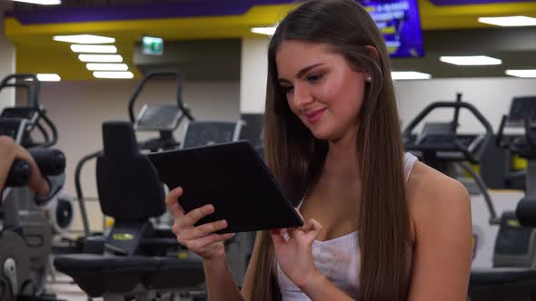 A Young Beautiful Woman Works on a Tablet in a Gym - Closeup