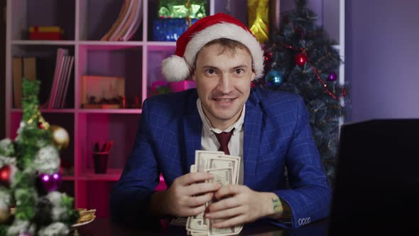 Happy Businessman in Santa Hat with Money Looking at Camera in Office