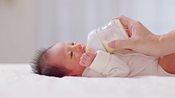 Close up hand of mother holding milk bottle Newborn baby lying on bed drinking milk