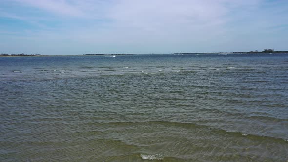 A low angle drone shot over a beach, looking out at the water & the horizon. It is at low tide on a