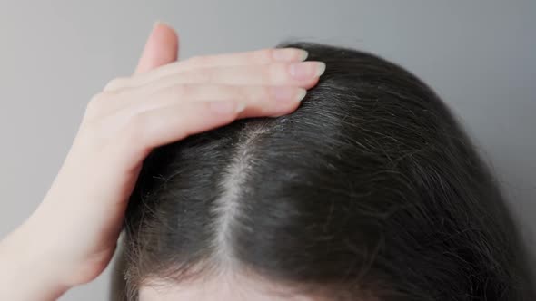 Close up of female's head. Woman dripping cosmetic oil on a hair parting and rubs it with fingers