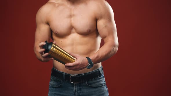 Topless athlete with flask. Muscular body of a sportsman isolated on red studio background.