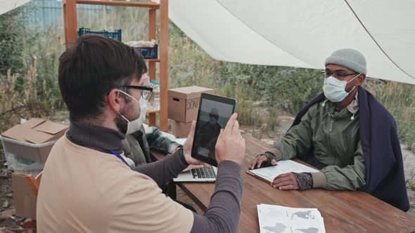 Social Worker Taking Photo of Refugee Man in Face Mask