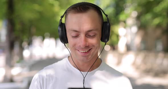 Smiling Man Takes Off a Big Headphones in the Summer City
