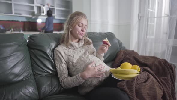 Portrait of Pretty Pregnant Caucasian Girl Eating Apple and Caressing Her Belly
