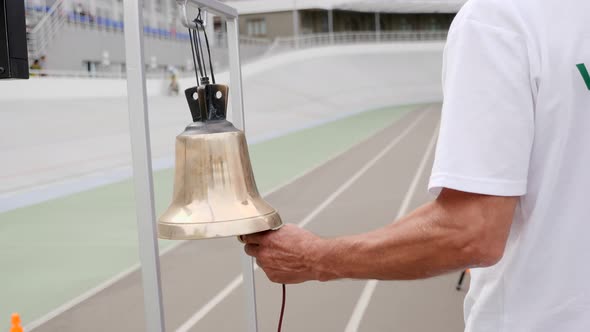 Cycling Referee Hand Rings the Bell on The Velodrome. Track Judge Ringing Golden Bell. Cycling Race