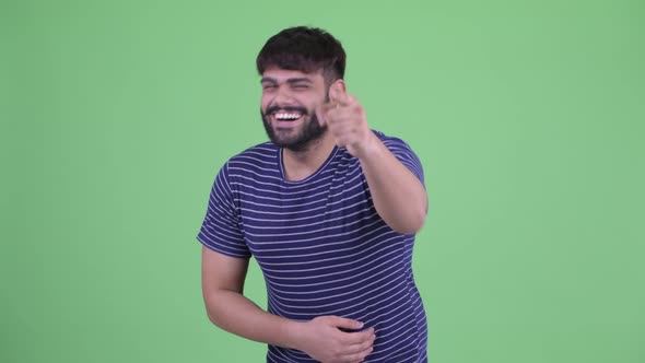 Happy Young Overweight Bearded Indian Man Laughing and Pointing at Camera